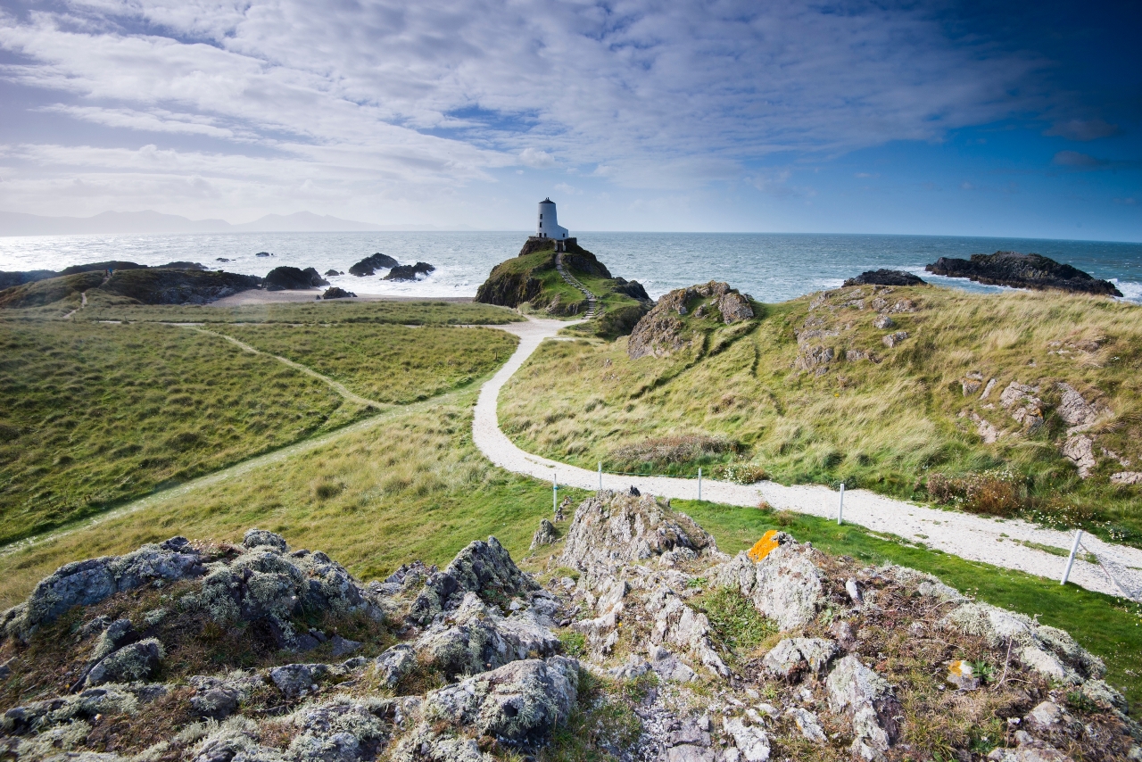 Curvy footpath leads to a white lighthouse looking over rocks to the Menai Straits in Wales (Image: GettyRF_593129203 - North Wales)